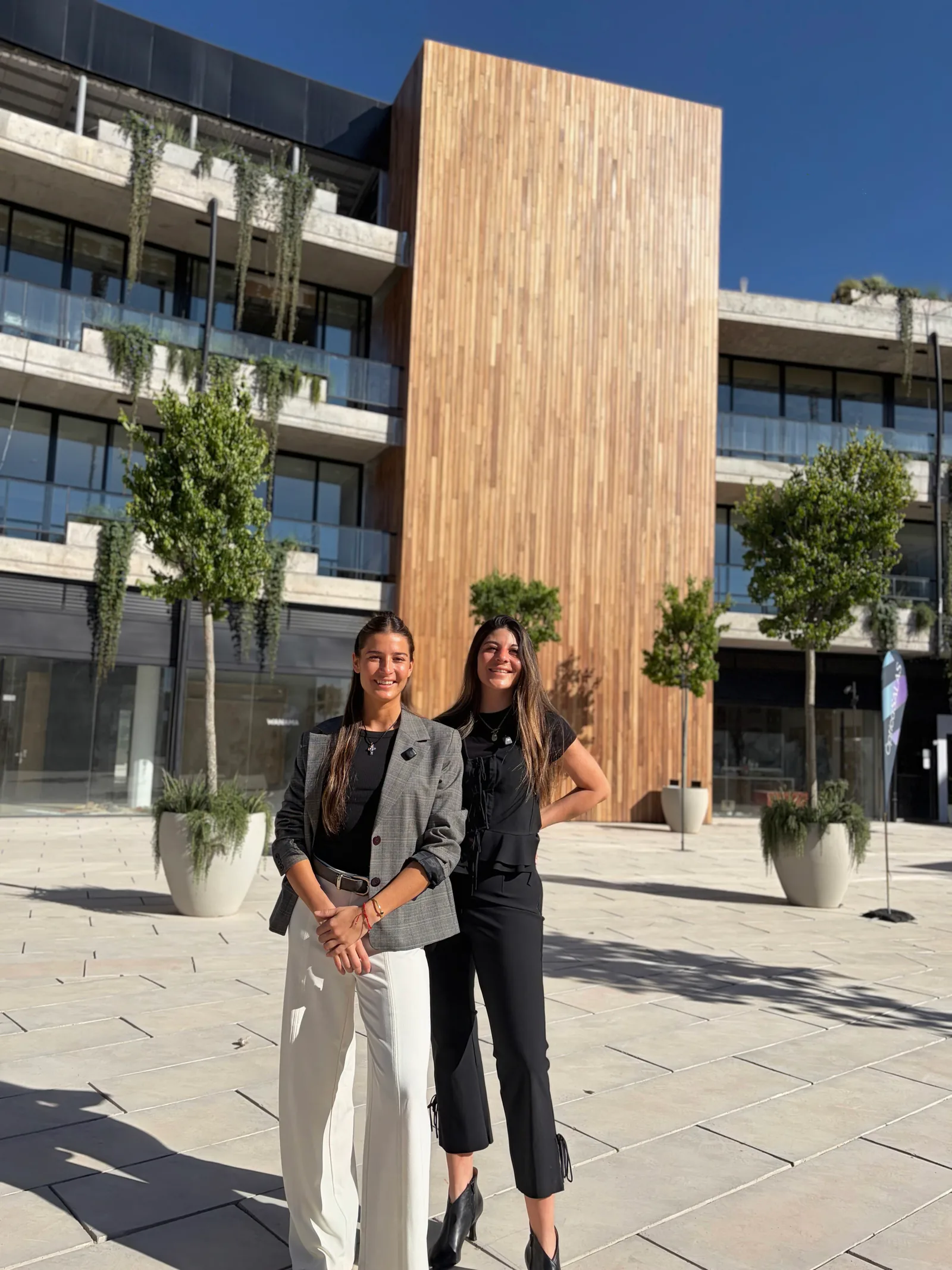 Dos integrantes de Mavenz frente al edificio de Espacio Mavenz, con la fachada de madera detrás