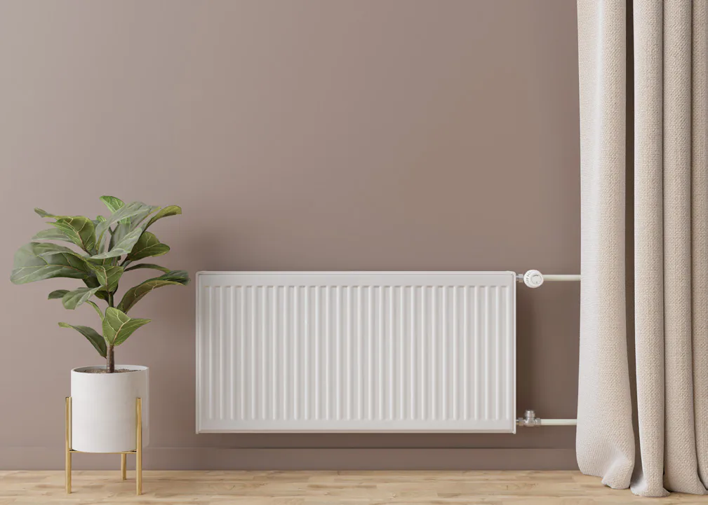 Radiador blanco de calefacción sobre una pared rosa viejo, con una planta en una maceta blanca y una cortina de lino