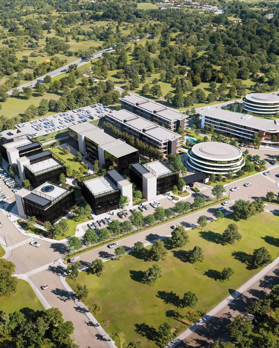Vista aérea del campus de WA Diamond entre árboles: bloques de oficinas vidriados, dos bloques largos de apartamentos y el edificio circular de los studios; al fondo, el edificio en curva de WA Well junto a otro edificio circular, con calles, cruces peatonales y estacionamientos alrededor.